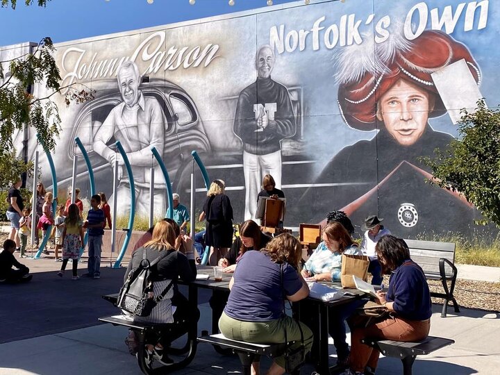 A group of people write at a picnic table in front of a mural