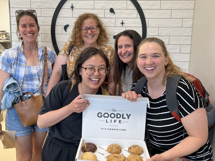 A group of co-directors stands around a box of cookies